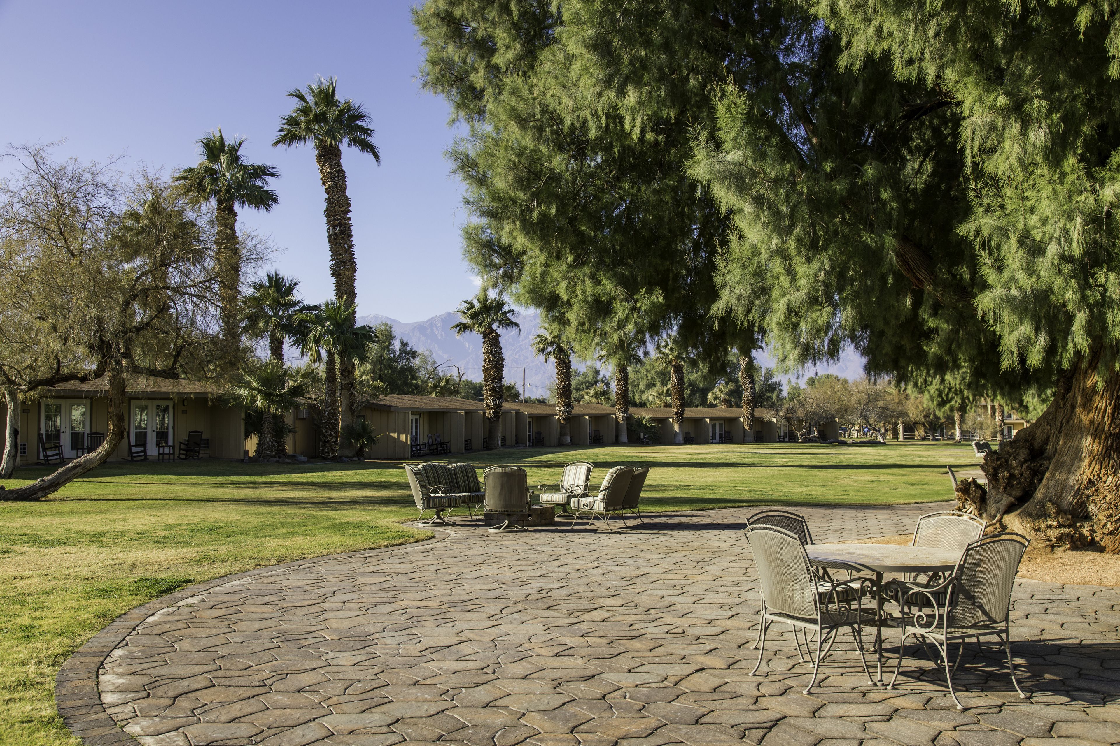 A patio area with stone flooring and metal furniture, surrounded by palm trees and a lawn.
