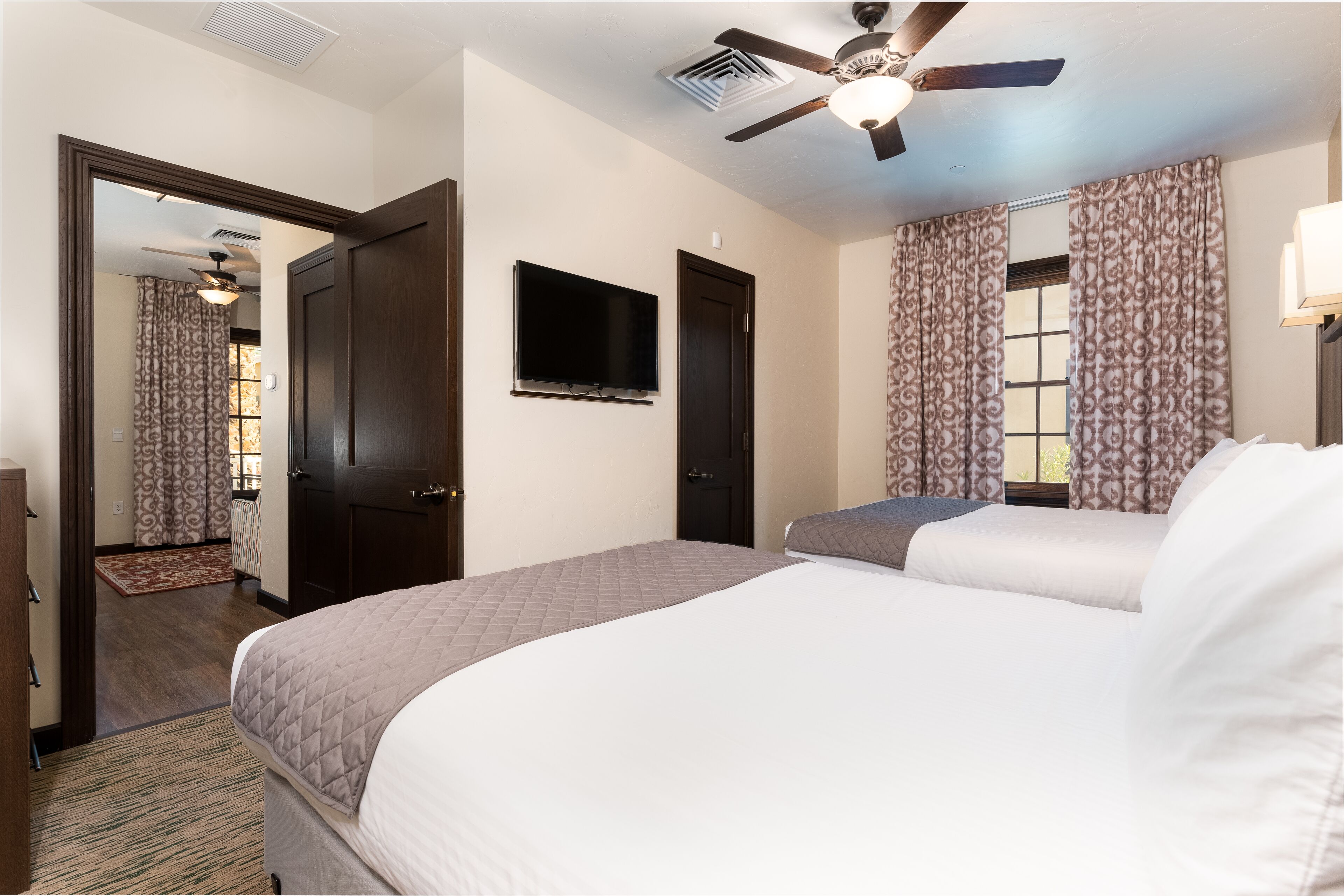 A hotel room with a bed, a ceiling fan, a TV, and patterned curtains.