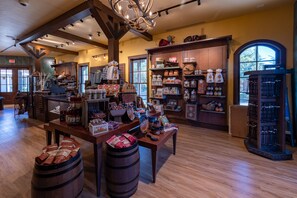 A spacious interior with wooden floors, a central table displaying various items, and shelves stocked with goods.