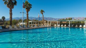 A clear blue pool with lounge chairs and palm trees, surrounded by mountains.