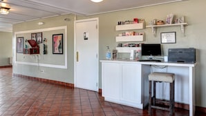A clean, well-lit hallway with a tiled floor, a reception desk with a computer and a printer, and a small stool. There are framed pictures on the wall and a door labeled "Restroom". - Fiddler's Inn (Nashville)
