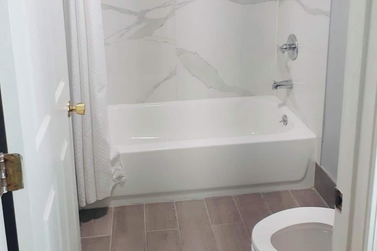 A bathroom with a marble wall, a bathtub, a toilet, and a shower.