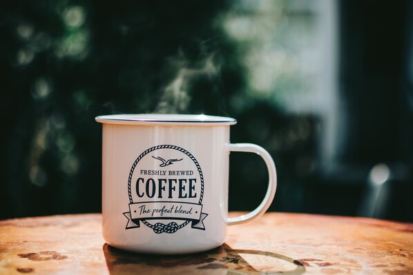 A white mug with a coffee design and steam rising from it. - Fiddler's Inn (Nashville)