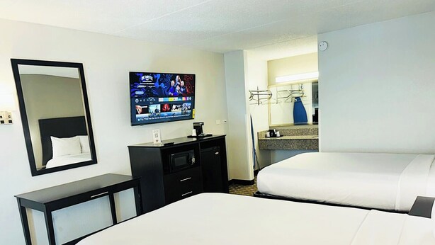 A hotel room with two beds, a TV mounted on the wall, a desk with a mirror, and a small kitchenette. - Fiddler's Inn (Nashville)