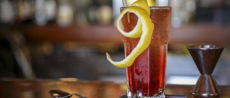 A glass of red beverage with a lemon slice and straw, placed on a coaster with a spoon beside it.