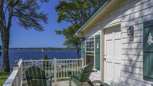 A wooden deck with two Adirondack chairs, a white garage door, and a view of the water.