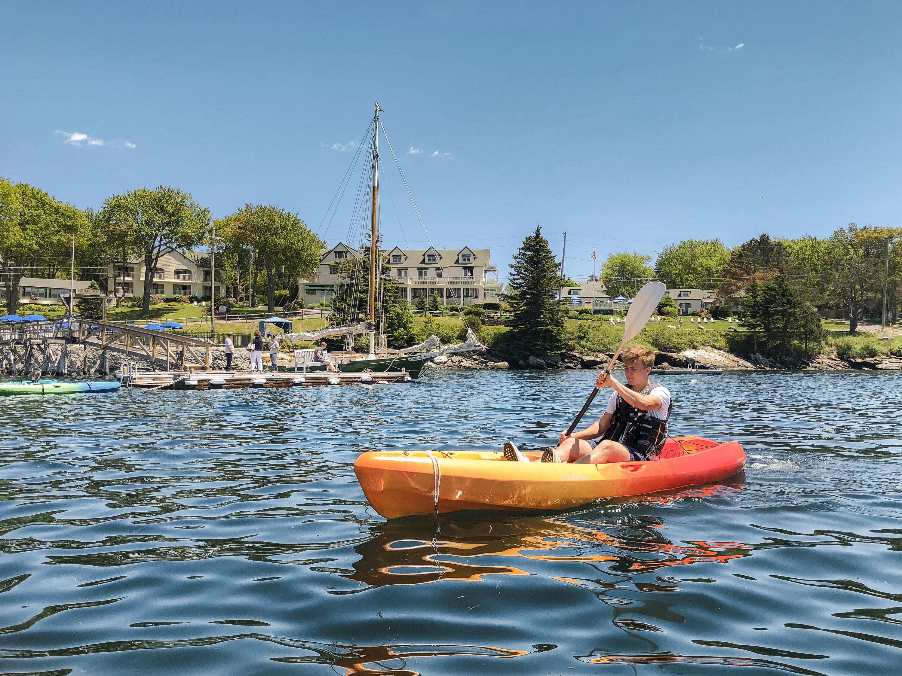 A person kayaking on a calm lake with a dock and buildings in the background.