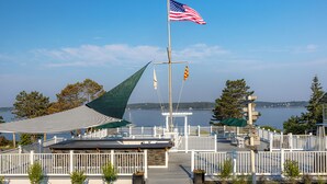 A waterfront deck with a flagpole, a covered seating area, and a view of the water.