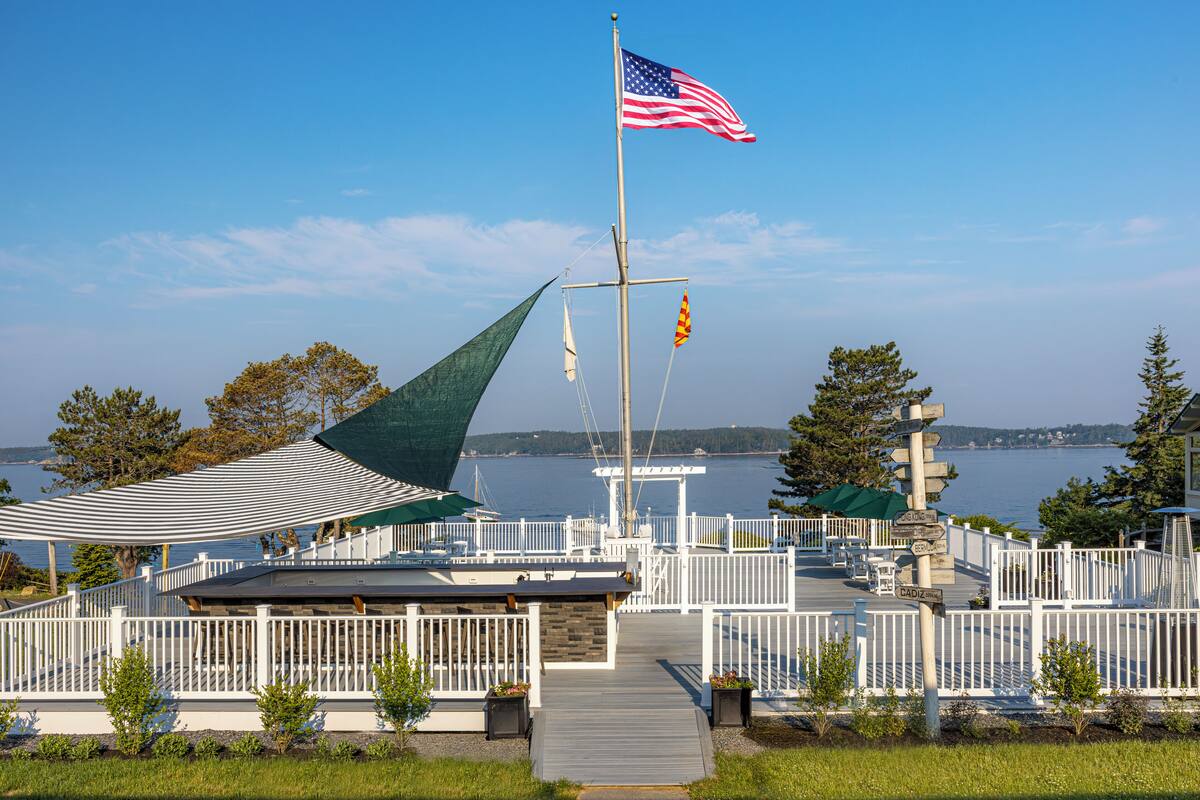 A waterfront deck with a flagpole, a covered seating area, and a view of the water.