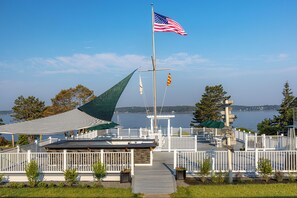 A waterfront deck with a flagpole, a covered seating area, and a view of the water.