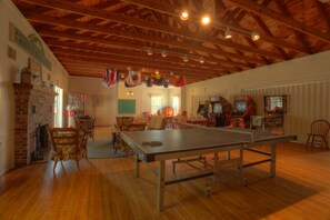 A spacious room with a ping pong table, wooden floors, and a brick fireplace.