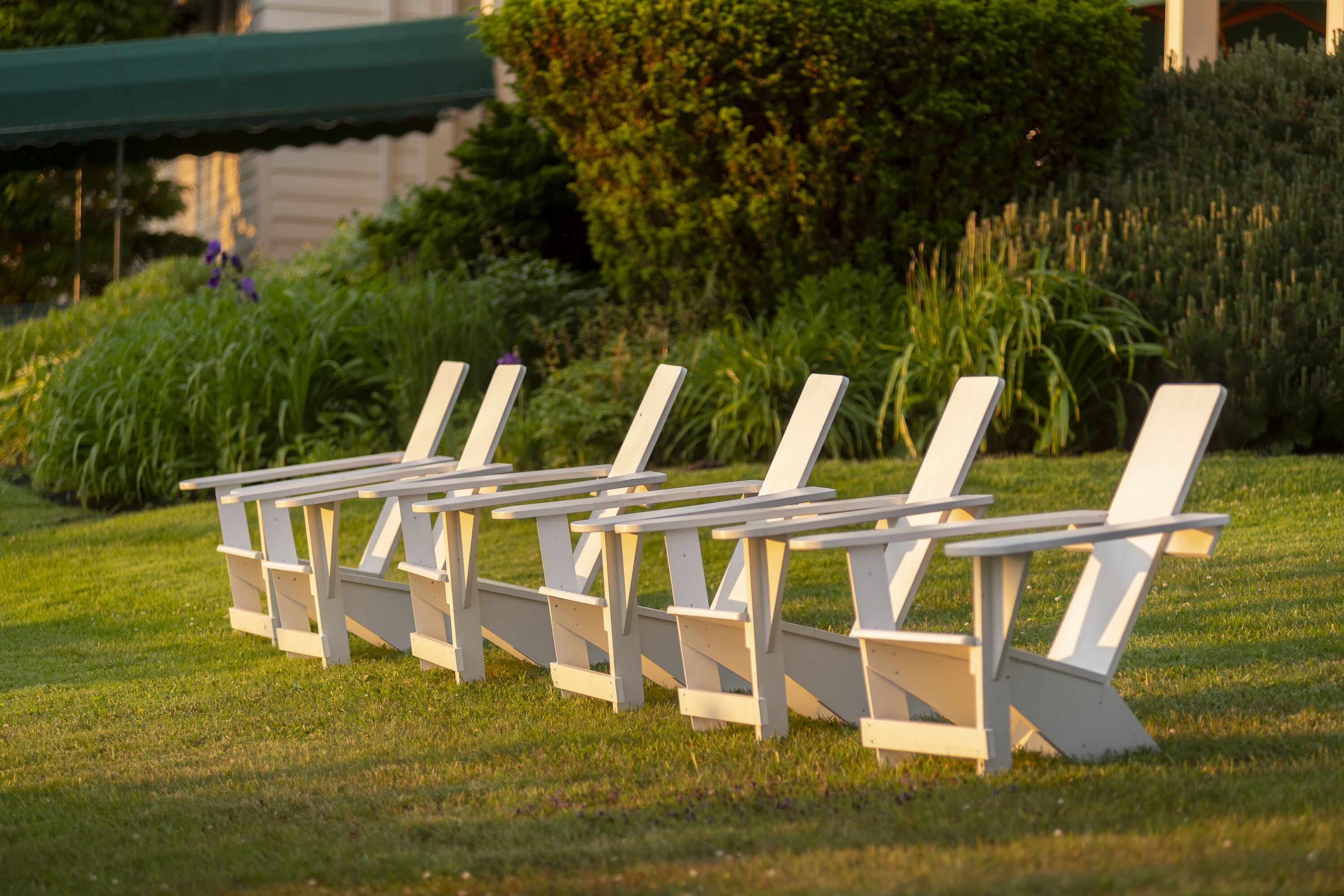 A row of white lounge chairs with attached tables, arranged on a grassy lawn.