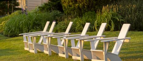 A row of white lounge chairs with attached tables, arranged on a grassy lawn.