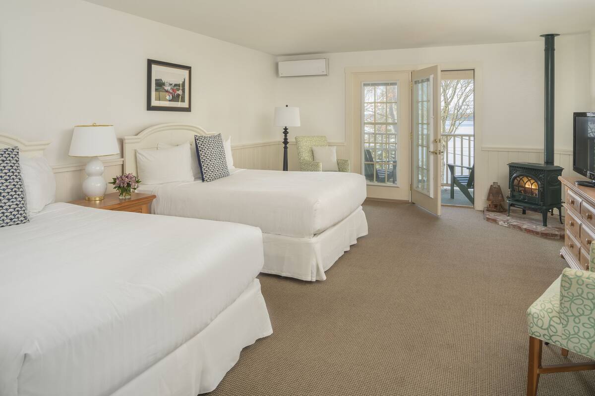A hotel room with two beds, a television, a fireplace, and a view of the outdoors.