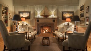 A cozy living room with a fireplace, two armchairs, a coffee table, and lamps. - Spruce Point Inn (Boothbay Harbor)