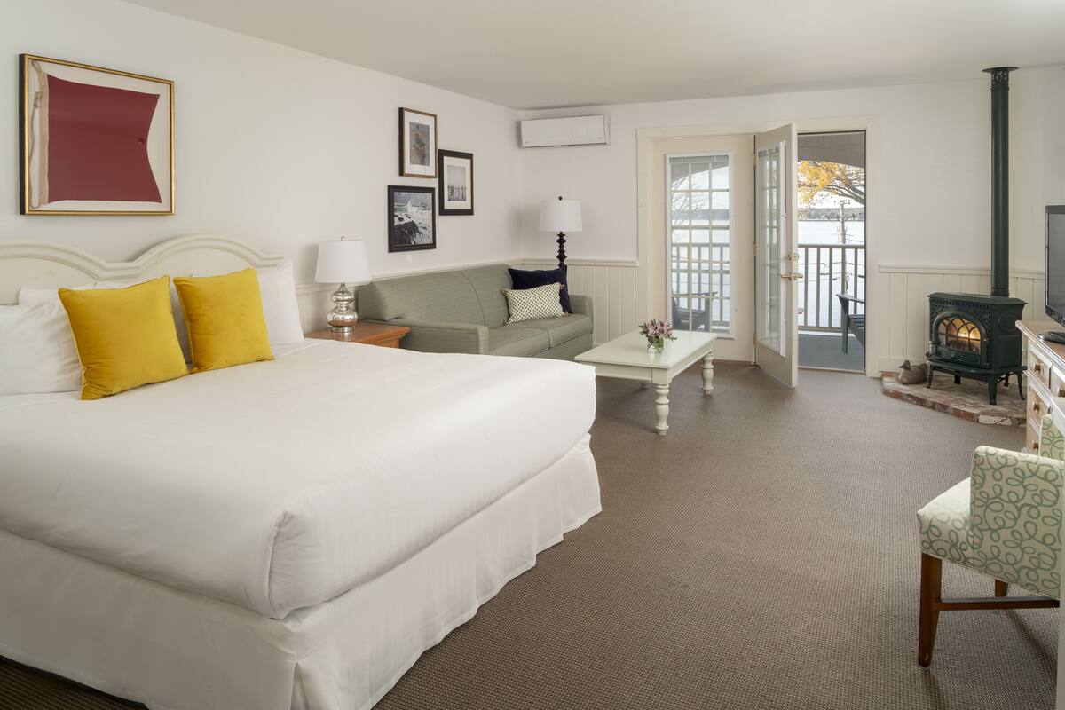 A hotel room with a large bed, a sofa, a small table, a television, and a fireplace.