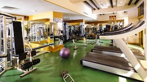 Academia com esteiras, máquinas de musculação e uma bola de exercícios grande.