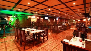 A restaurant with a tiled floor, wooden tables and chairs, and a grid-patterned ceiling. - Baisan International Hotel (Manama)