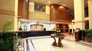 A hotel lobby with a reception desk, a large decorative table, and potted plants. - Baisan International Hotel (Manama)