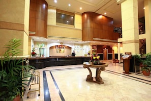 A hotel lobby with a reception desk, a large decorative table, and potted plants. - Baisan International Hotel (Manama)
