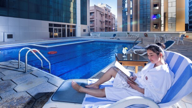A poolside area with lounge chairs, a swimming pool, and modern buildings in the background. - Baisan International Hotel (Manama)