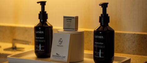 A bathroom counter with two Lather hand wash bottles, a shower cap, and a face soap box.