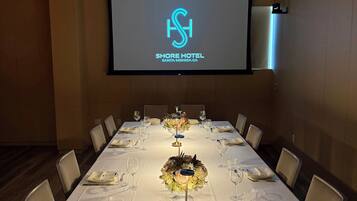 Ein Konferenzraum mit langem Tisch für eine Besprechung, einem Bildschirm, der den Hotelnamen zeigt, und einem modernen Deckengestaltung.