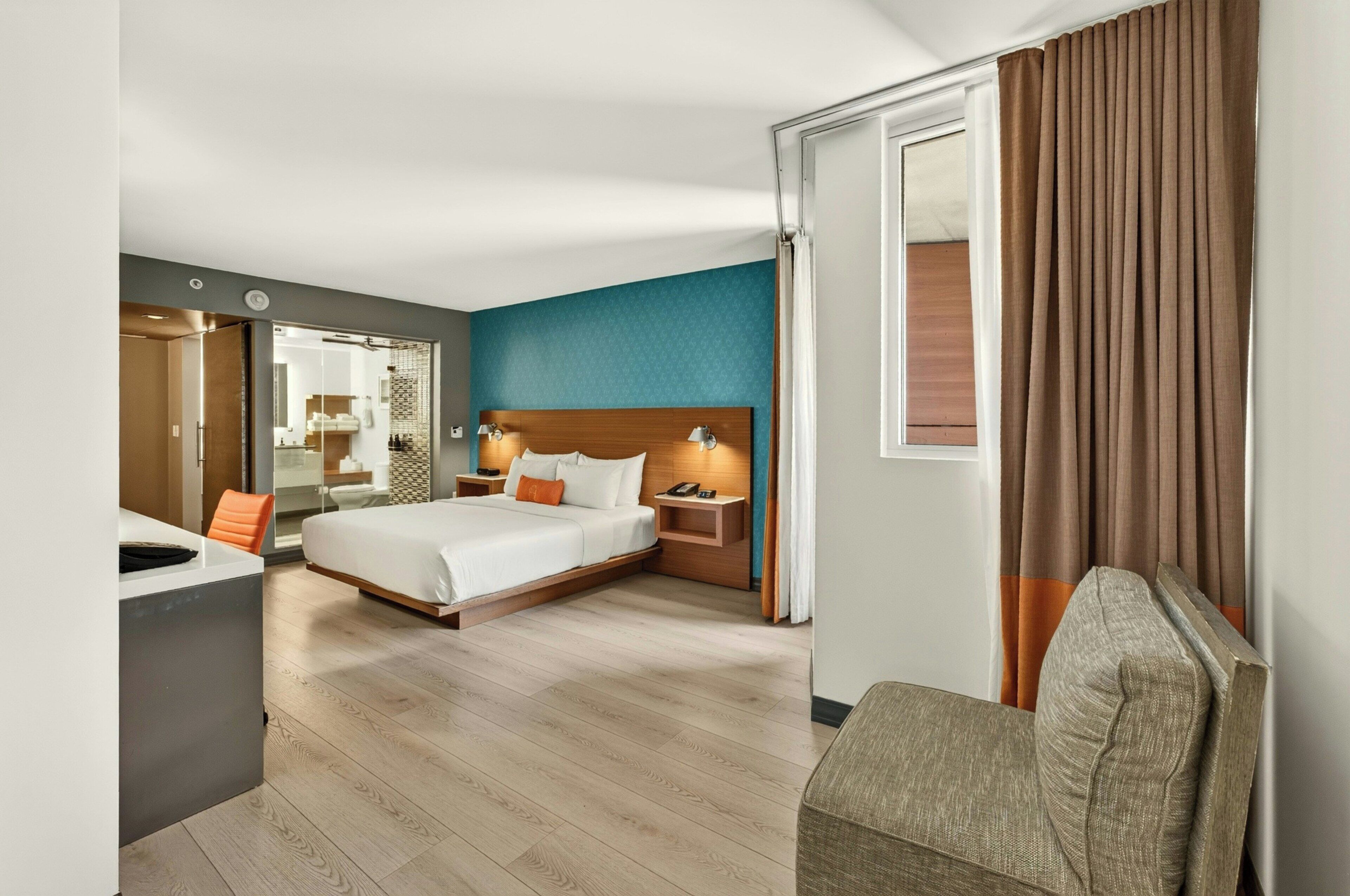 Una habitación de hotel con una cama, mesitas de noche, un escritorio, una silla y un baño visible a través de una puerta abierta.