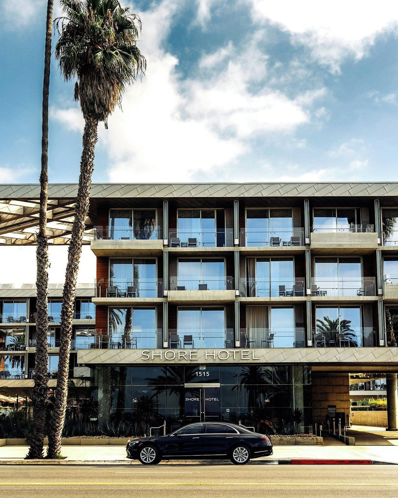 Um hotel de vários andares com design arquitetônico moderno, apresentando uma entrada imponente e um carro estacionado em frente.