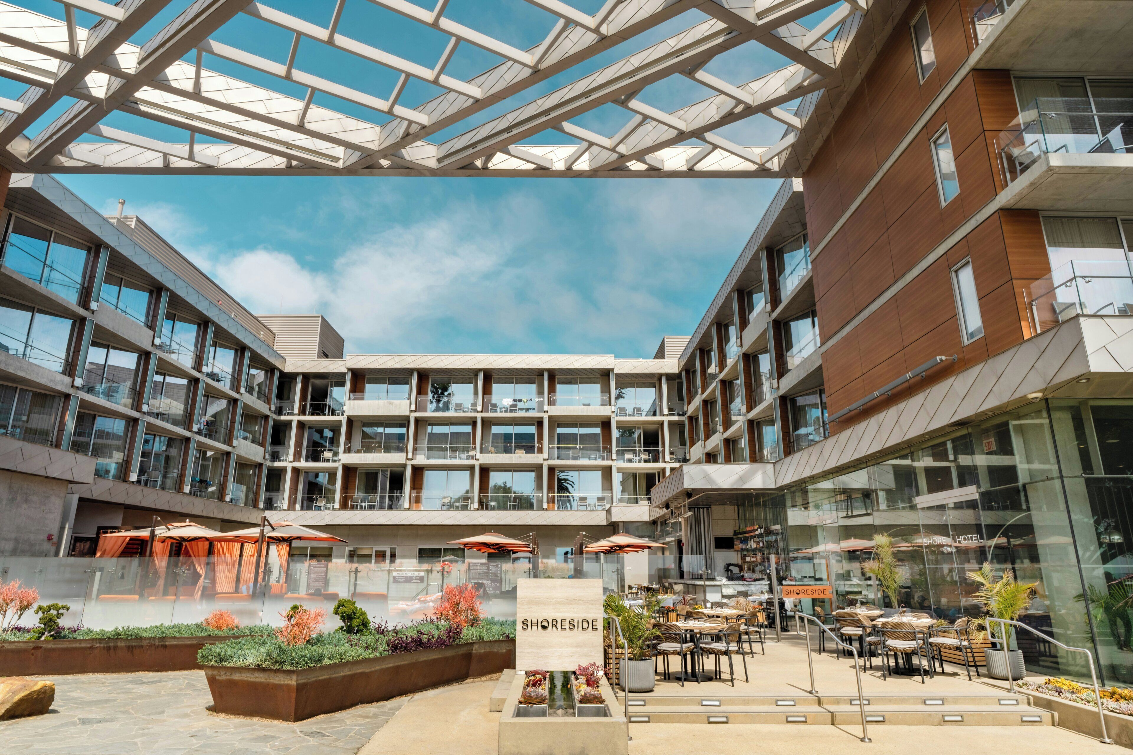 A hotel atrium with a glass ceiling, outdoor seating, and a sign reading 'SHORESIDE'.