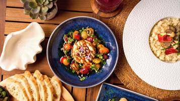 A dining table with various dishes, including a blue bowl with a salad, a plate of sliced bread, and a white plate with rice and mushrooms.