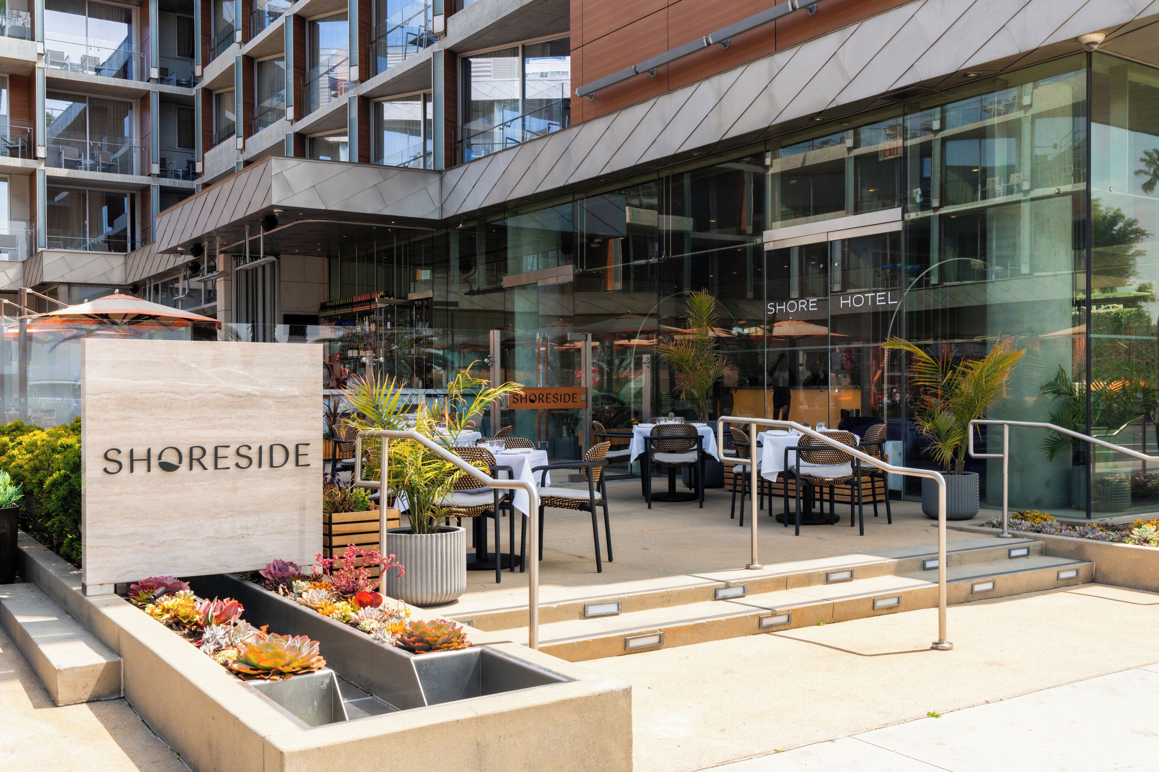 A hotel exterior with outdoor seating, a sign reading 'SHORESIDE HOTEL,' and a modern building facade.