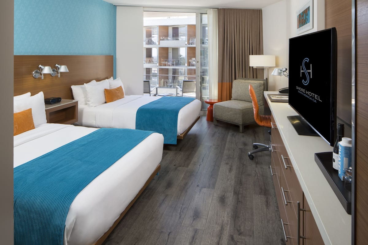 Habitación de hotel con dos camas, televisión, escritorio y vista a la ciudad.