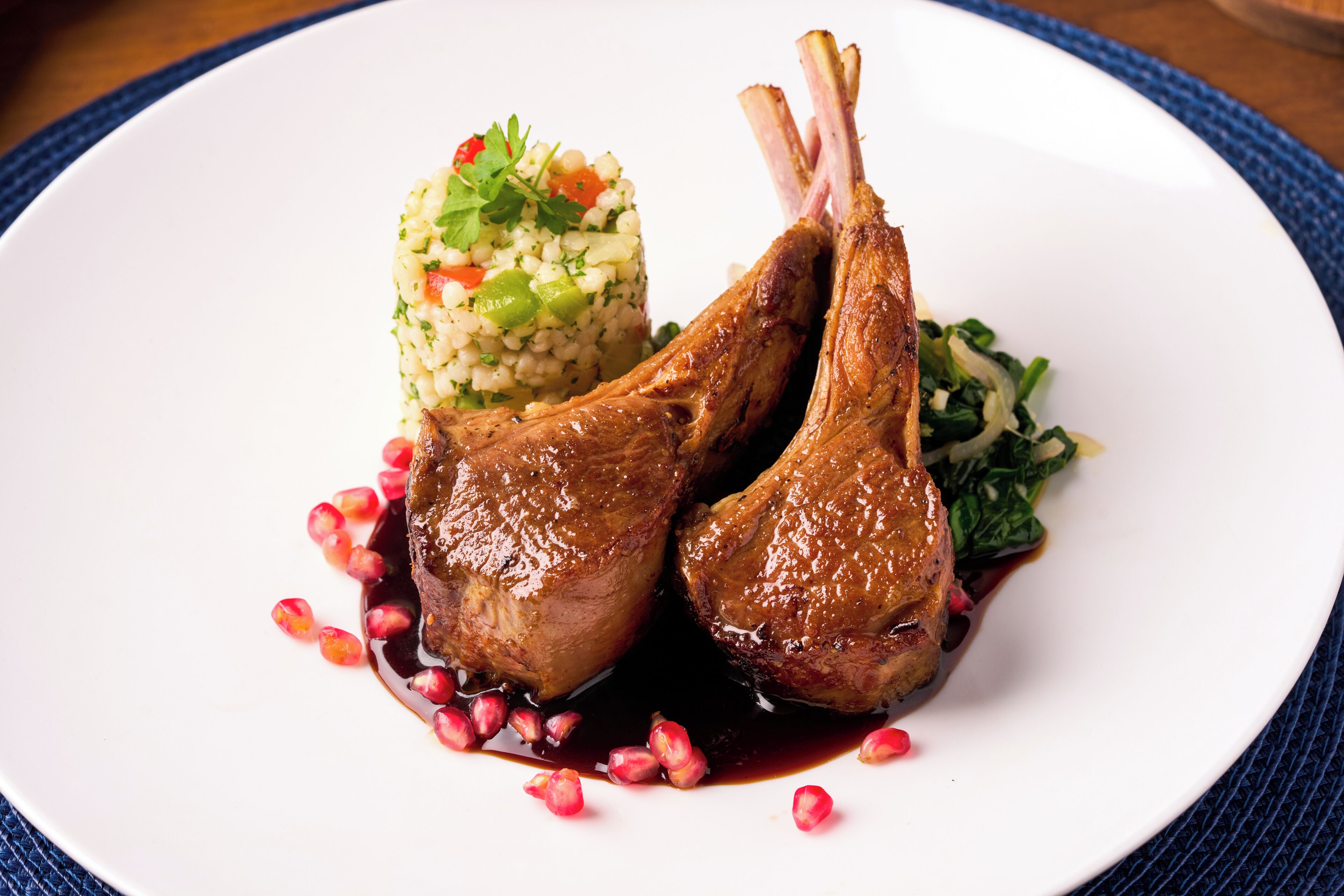 A plate with two lamb chops, couscous, and greens.