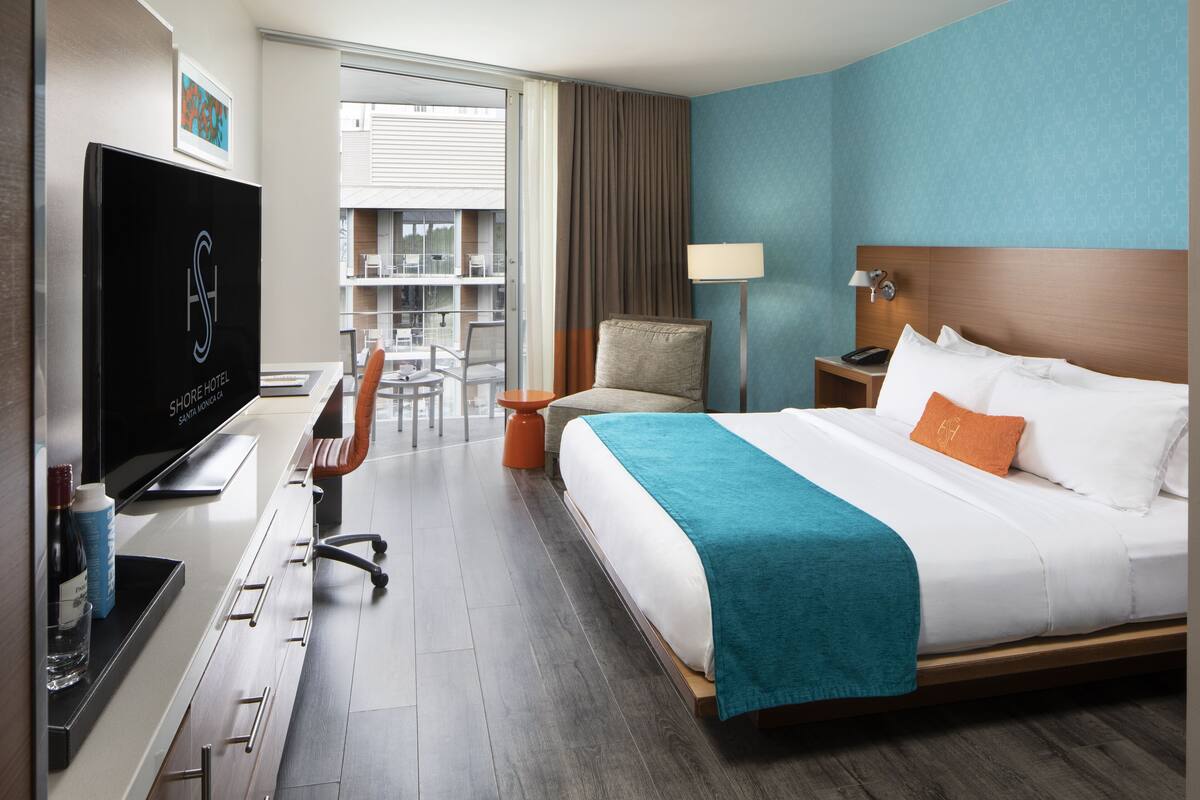 Habitación de hotel con cama, escritorio, silla, televisor y ventana con vistas al exterior.