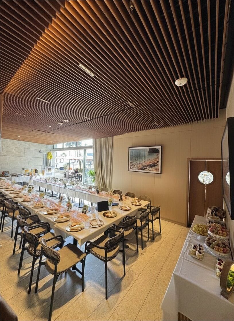 A long dining table set with chairs, a buffet table with food, and a ceiling with a unique slatted design.