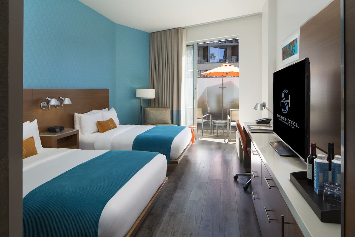 Habitación de hotel con dos camas, televisión, escritorio y balcón con sombrilla.