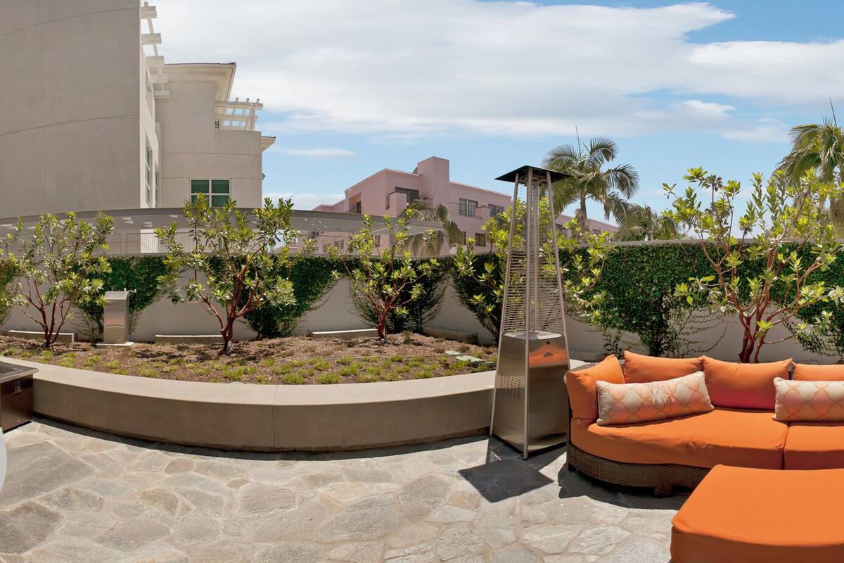Un patio de hotel moderno con mesas al aire libre, un jardín central y una zona de piscina.