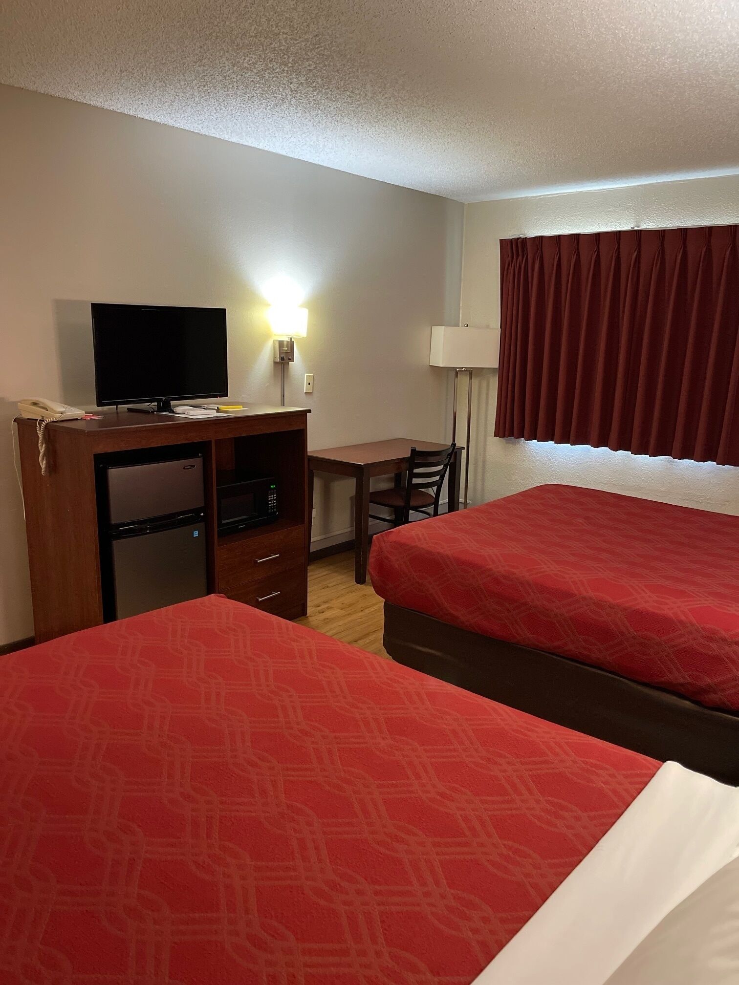 A hotel room with two single beds, a desk with a TV, a phone, and a lamp.