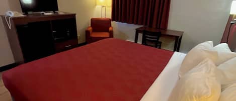 Une chambre d’hôtel avec un grand lit, un téléviseur posé sur un meuble, un bureau, une chaise et un appareil de climatisation.