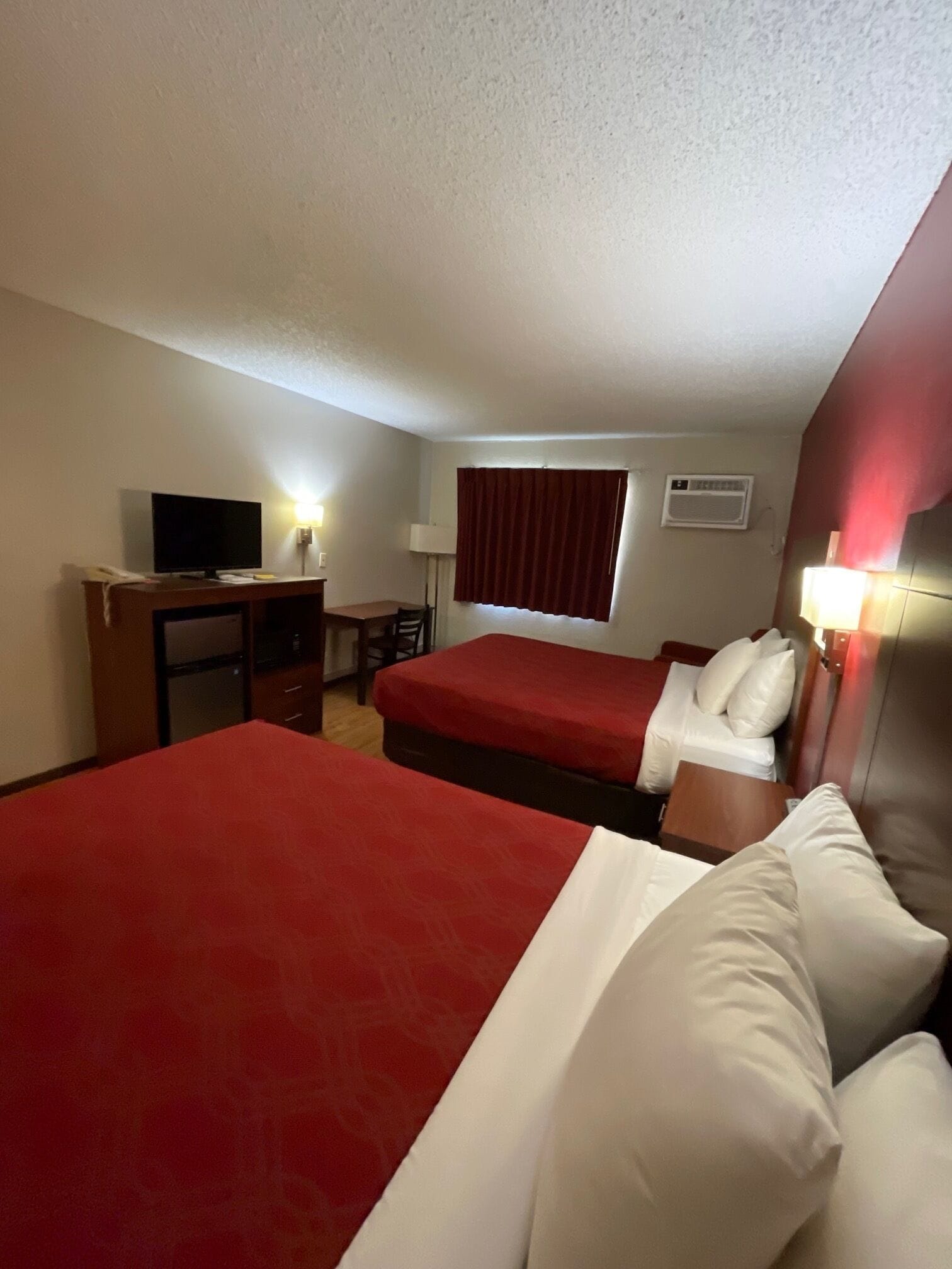 Una habitación de hotel con dos camas, un escritorio, un televisor y una ventana con cortinas.