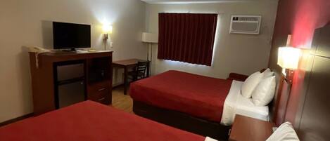 A hotel room with two beds, a desk, a television, and a window with curtains.