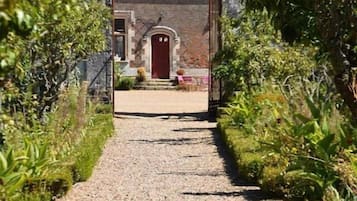 A gravel pathway leading to a stone building with a red door, surrounded by greenery.