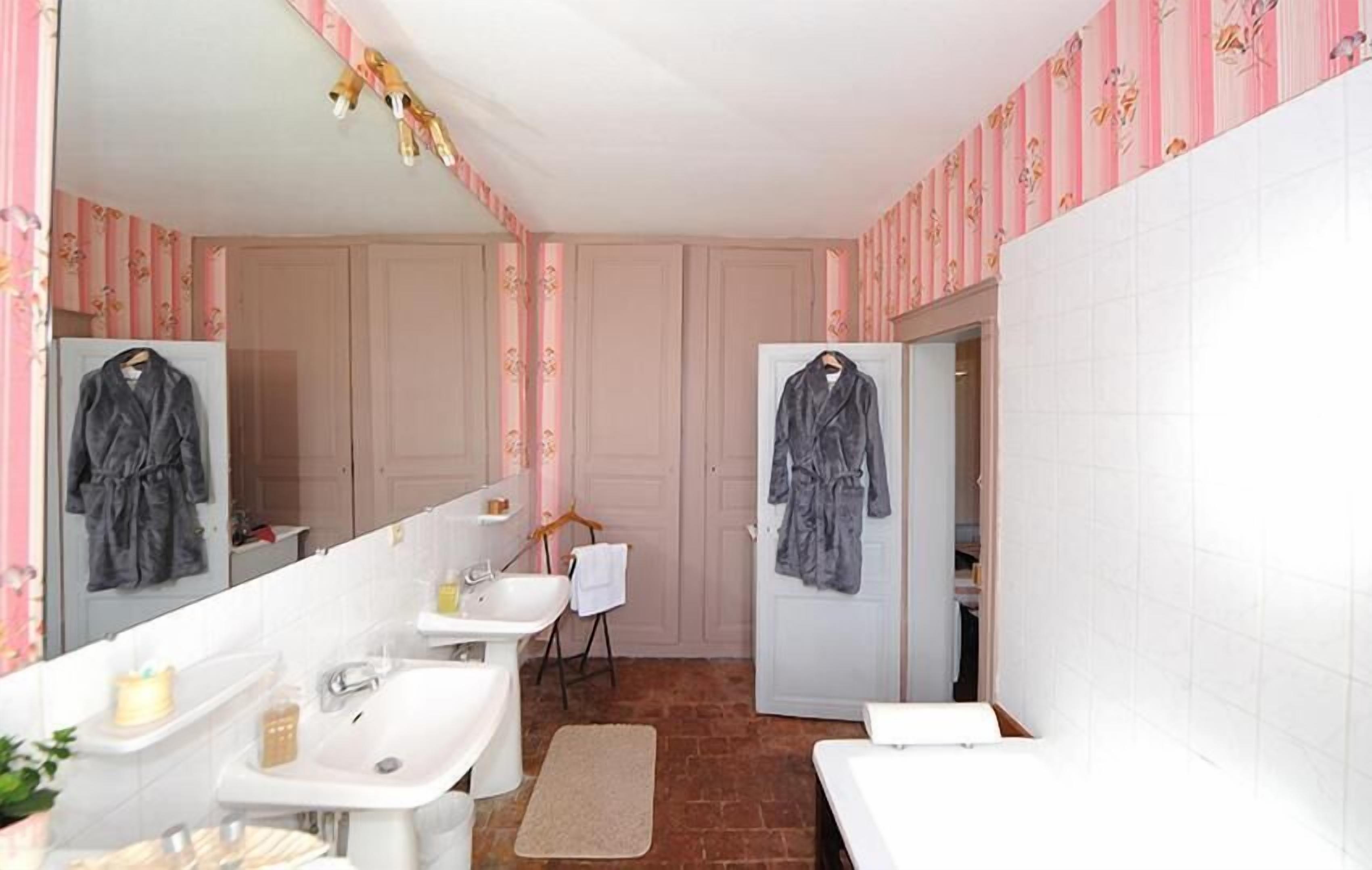 Un baño con dos lavamanos, un espejo, un perchero para toallas y una puerta que da a otra habitación.