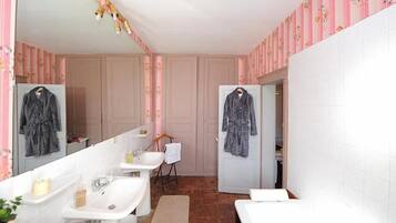 Un baño con dos lavamanos, un espejo, un perchero para toallas y una puerta que da a otra habitación.