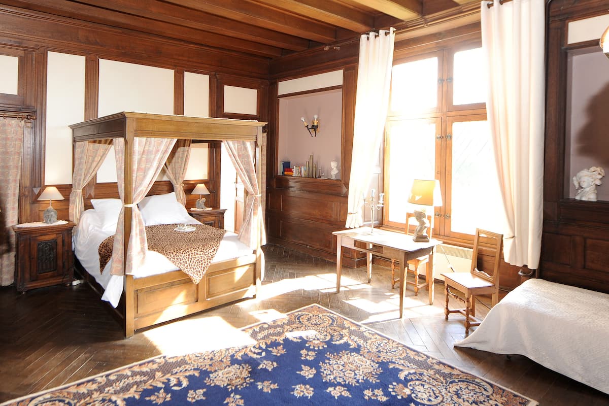 A traditional wooden bedroom with a four-poster bed, a desk, and a chair.