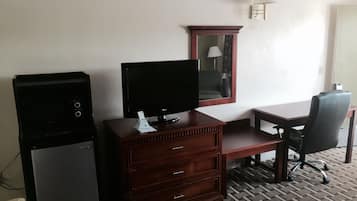 A hotel room with a TV, a wooden dresser, a desk, a chair, and a lamp.