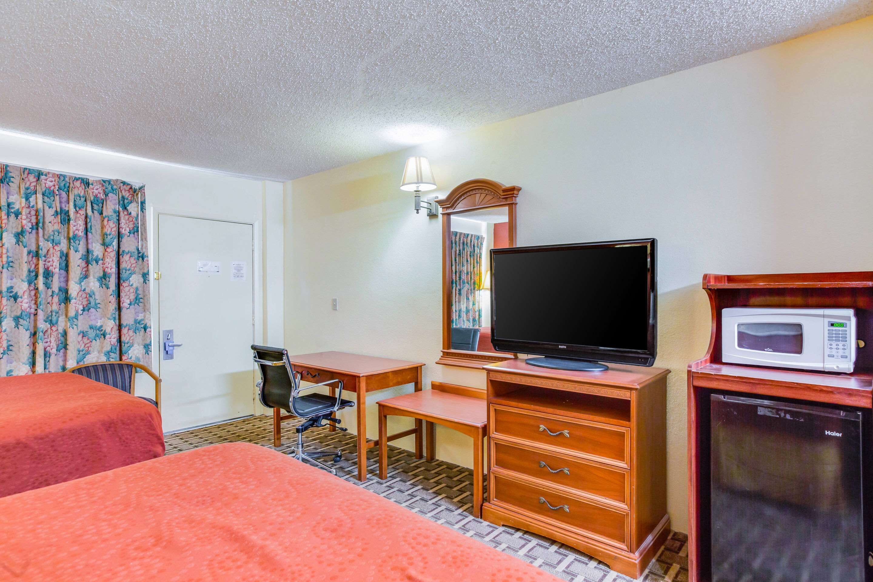 A hotel room with two beds, a desk, a television, a microwave, and a refrigerator.