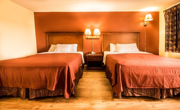 A hotel room with two beds, wooden headboards, a nightstand with lamps, and a patterned curtain.