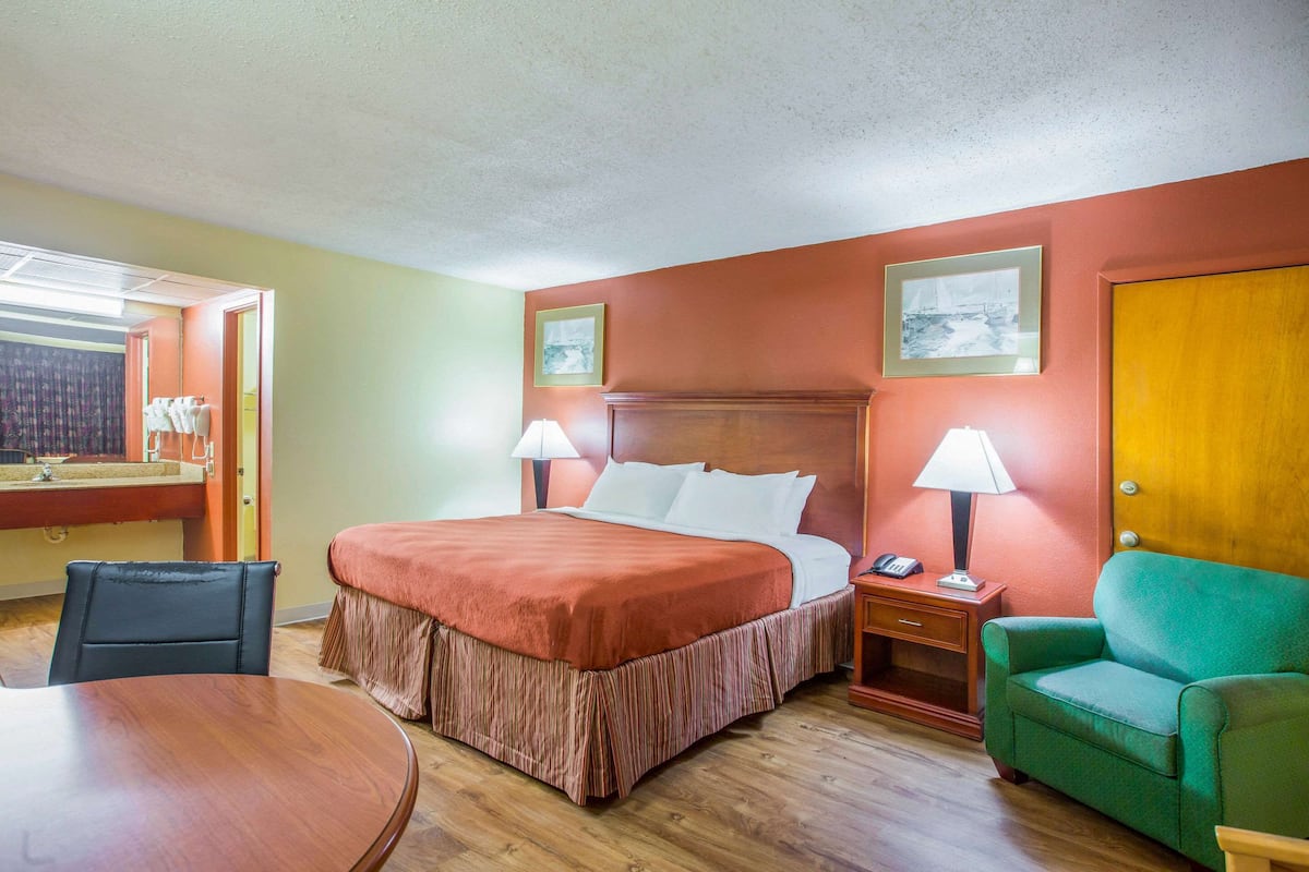 Una camera d'albergo con un letto, una sedia, un tavolo e una scrivania con una lampada.
